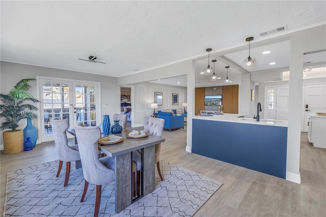 dining area with light wood-style flooring, visible vents, a textured ceiling, and french doors