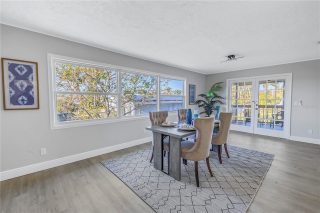 dining space with a textured ceiling, french doors, wood finished floors, and baseboards