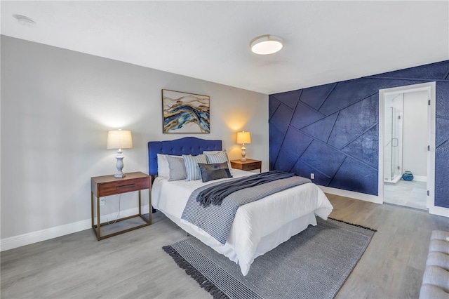 bedroom with an accent wall, baseboards, and wood finished floors