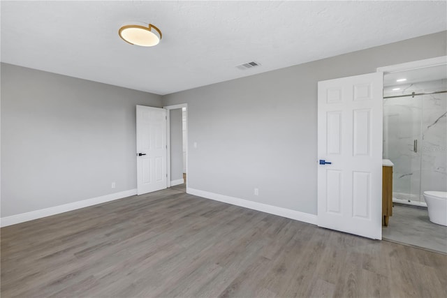 unfurnished bedroom featuring light wood-style flooring, connected bathroom, visible vents, and baseboards