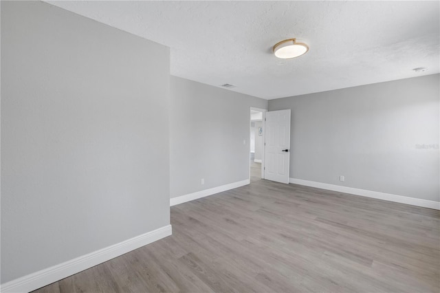 empty room featuring light wood-style floors, baseboards, and a textured ceiling