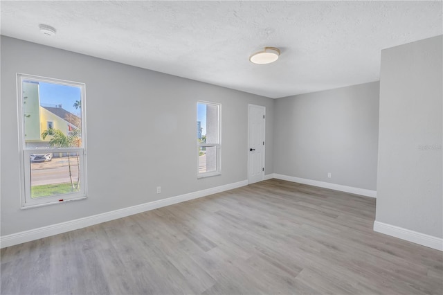 unfurnished room with plenty of natural light, light wood finished floors, baseboards, and a textured ceiling