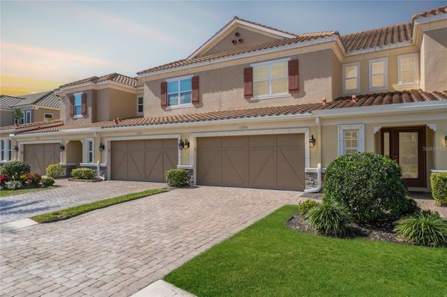 view of front of home with stucco siding, decorative driveway, an attached garage, and a tile roof