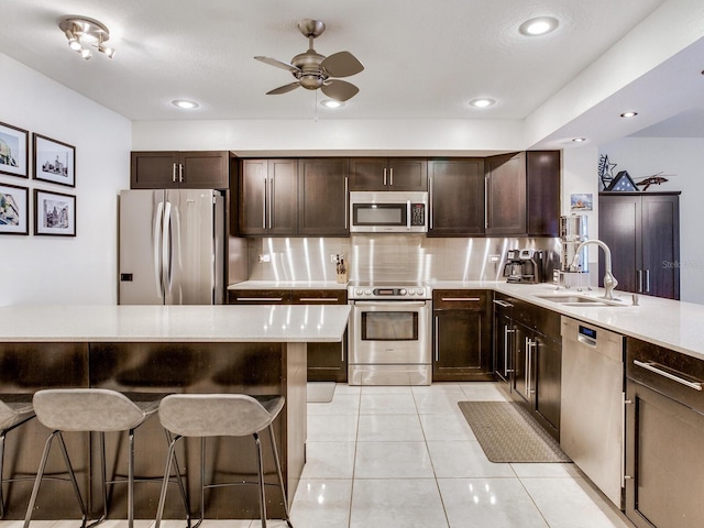 kitchen featuring a ceiling fan, a breakfast bar area, appliances with stainless steel finishes, light countertops, and a sink