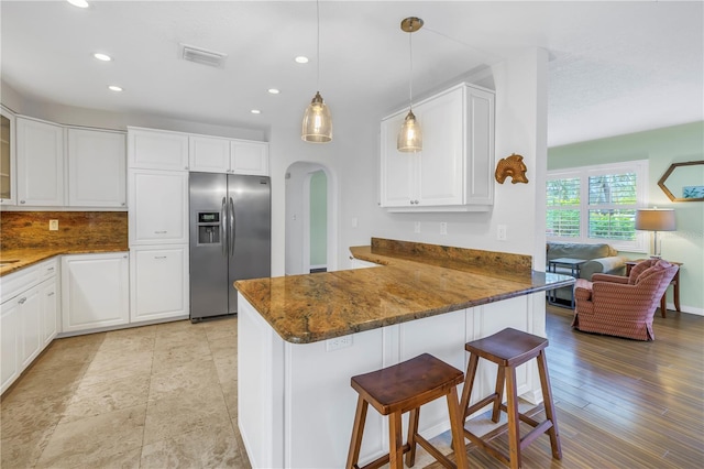 kitchen featuring arched walkways, white cabinets, stainless steel fridge with ice dispenser, a kitchen breakfast bar, and a peninsula