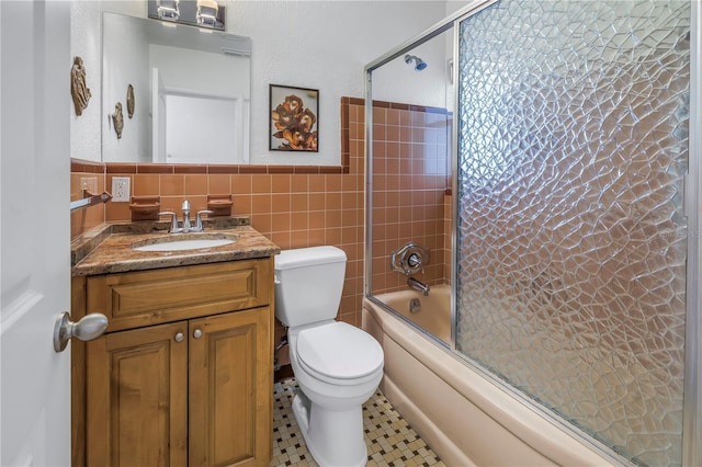 bathroom featuring toilet, shower / bath combination with glass door, vanity, tile walls, and wainscoting