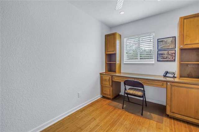 office featuring light wood-style floors, built in desk, baseboards, and a ceiling fan