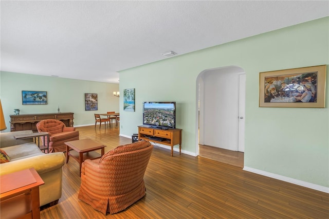 living room featuring arched walkways, visible vents, baseboards, and wood finished floors