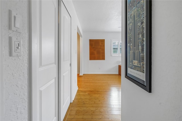 hall featuring a textured ceiling, light wood-style flooring, and baseboards