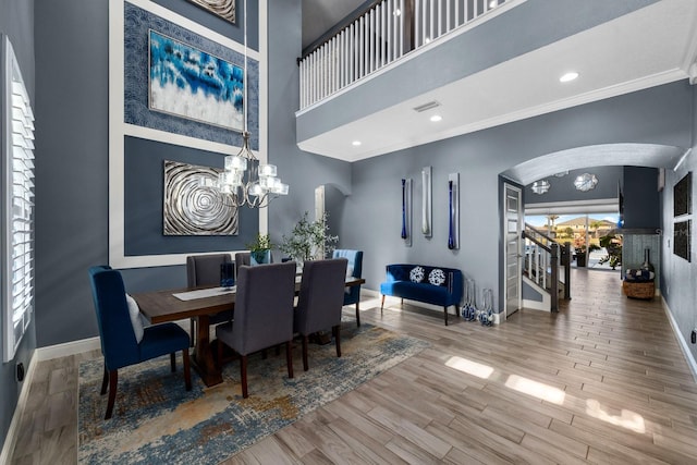 dining space with crown molding, wood-type flooring, a chandelier, and a high ceiling