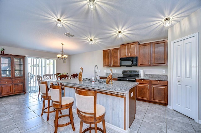 kitchen with pendant lighting, a breakfast bar, black appliances, an island with sink, and a chandelier