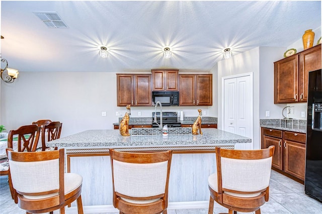 kitchen featuring light tile patterned flooring, a chandelier, a kitchen breakfast bar, black appliances, and a center island with sink