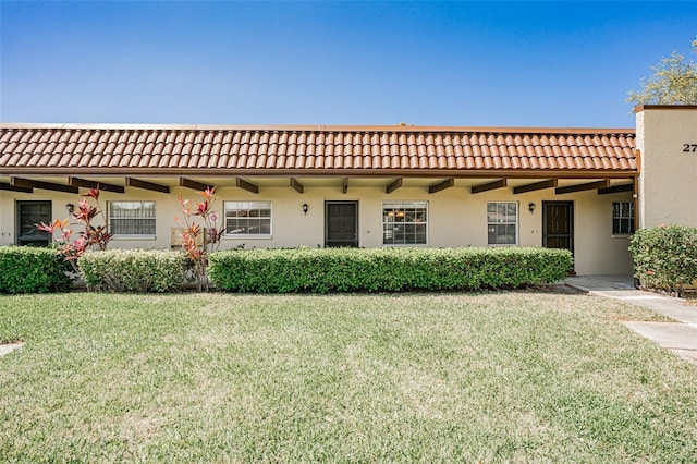 rear view of property with a tile roof, a yard, and stucco siding