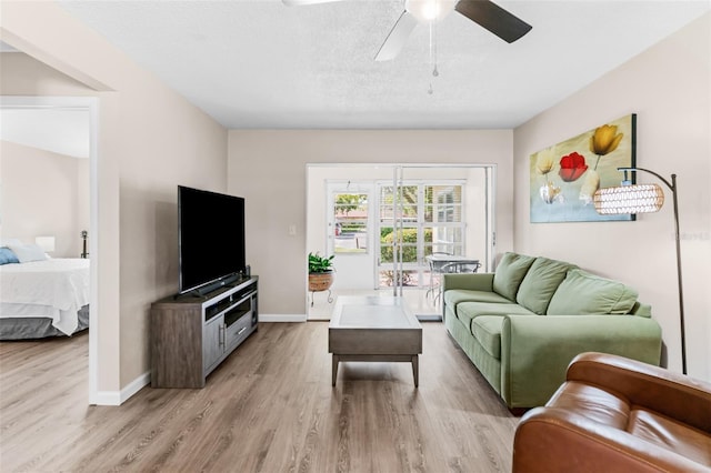 living room featuring a textured ceiling, a ceiling fan, light wood-type flooring, and baseboards