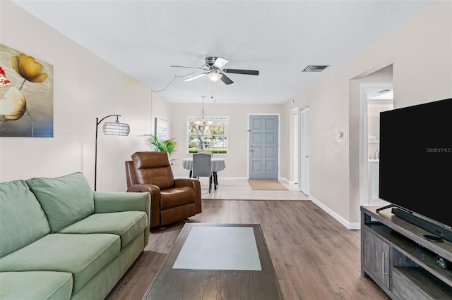 living area with wood finished floors, ceiling fan with notable chandelier, visible vents, and baseboards