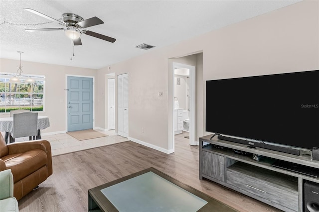 living room featuring visible vents, baseboards, wood finished floors, a textured ceiling, and a ceiling fan