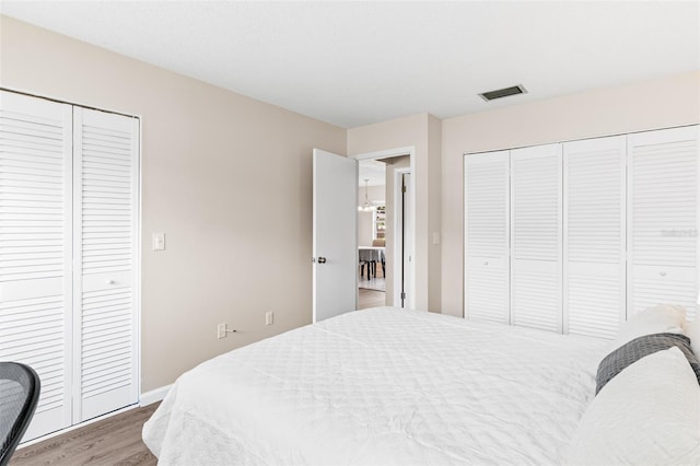 bedroom with visible vents, two closets, baseboards, and wood finished floors