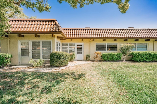 back of property featuring stucco siding, a tile roof, and a yard