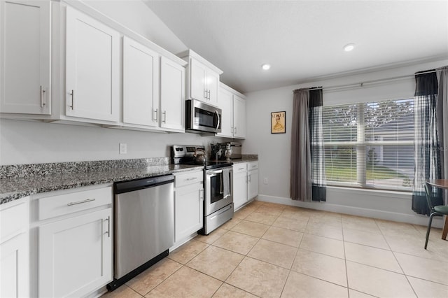 kitchen featuring white cabinetry, appliances with stainless steel finishes, light tile patterned floors, and dark stone countertops