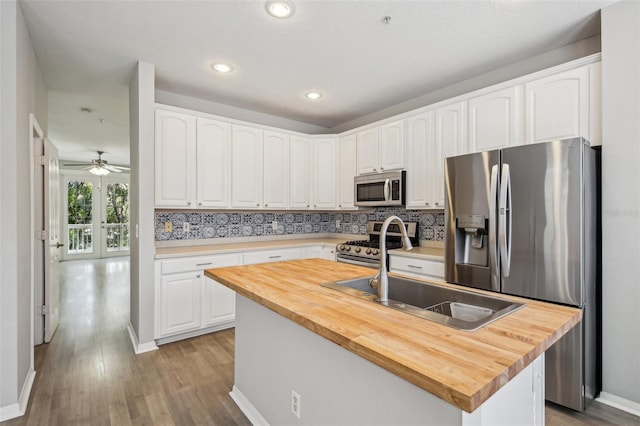 kitchen featuring butcher block counters, appliances with stainless steel finishes, a kitchen island with sink, a sink, and white cabinetry