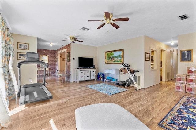 exercise area featuring ceiling fan, light wood-type flooring, and brick wall