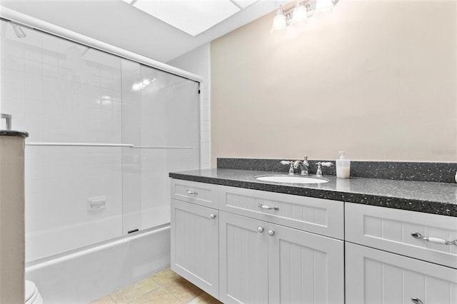 full bathroom with tile patterned flooring, toilet, a skylight, vanity, and bath / shower combo with glass door