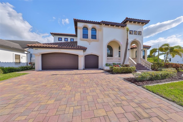 mediterranean / spanish-style house with a garage, decorative driveway, a tiled roof, and stucco siding