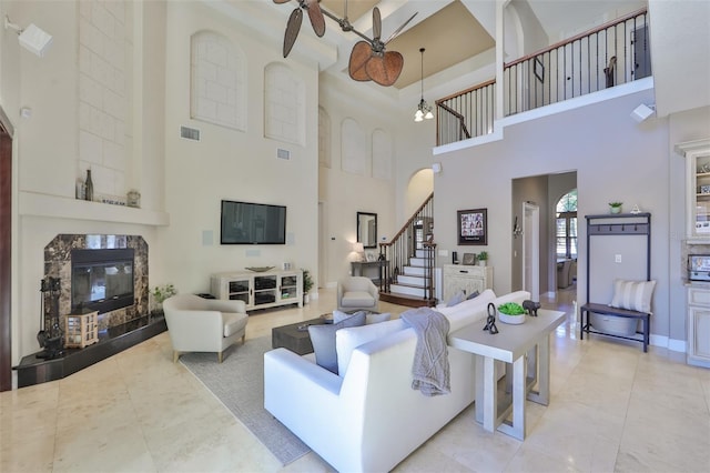 living room featuring a ceiling fan, visible vents, a high ceiling, a tiled fireplace, and stairs