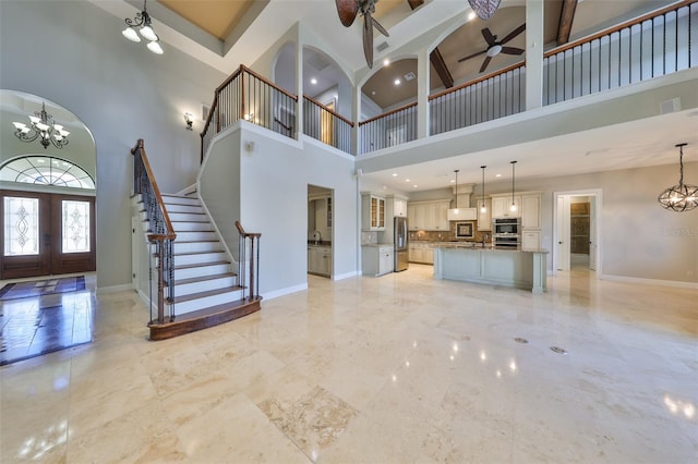 unfurnished living room with ceiling fan with notable chandelier, a towering ceiling, visible vents, french doors, and baseboards