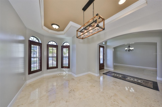 foyer entrance featuring an inviting chandelier, a tray ceiling, arched walkways, ornamental molding, and marble finish floor