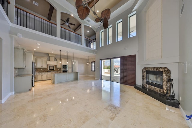 unfurnished living room featuring ceiling fan, a high ceiling, marble finish floor, a premium fireplace, and baseboards