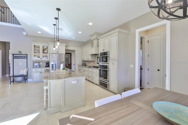 kitchen with tasteful backsplash, a warming drawer, appliances with stainless steel finishes, a sink, and a center island with sink