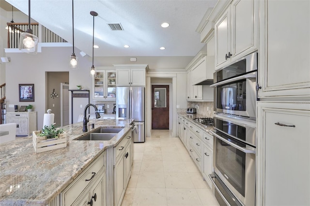 kitchen with glass insert cabinets, visible vents, a sink, appliances with stainless steel finishes, and decorative backsplash