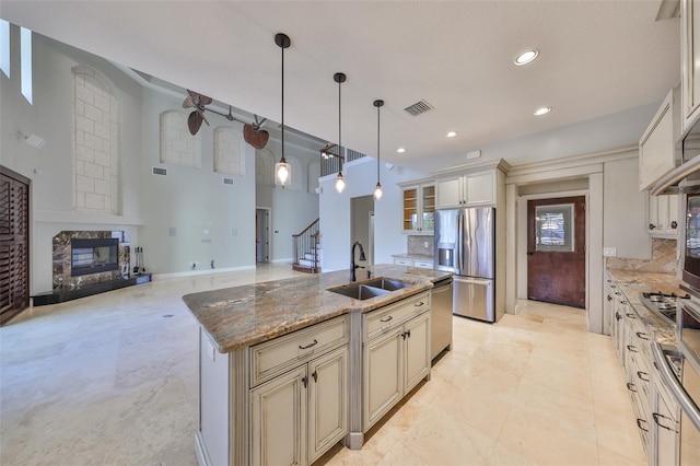 kitchen featuring cream cabinetry, visible vents, stainless steel appliances, a high end fireplace, and a sink