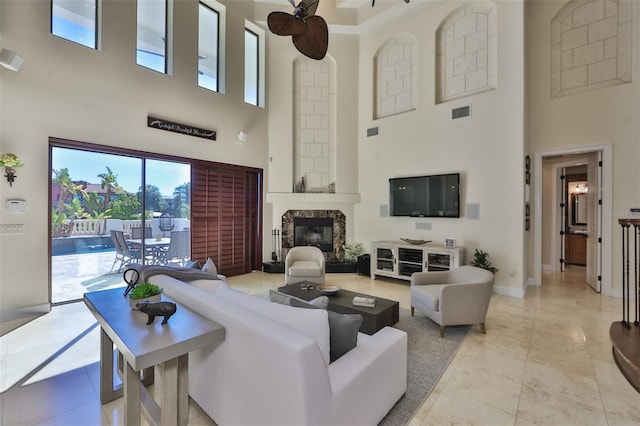 living room featuring a fireplace, a towering ceiling, a ceiling fan, visible vents, and baseboards
