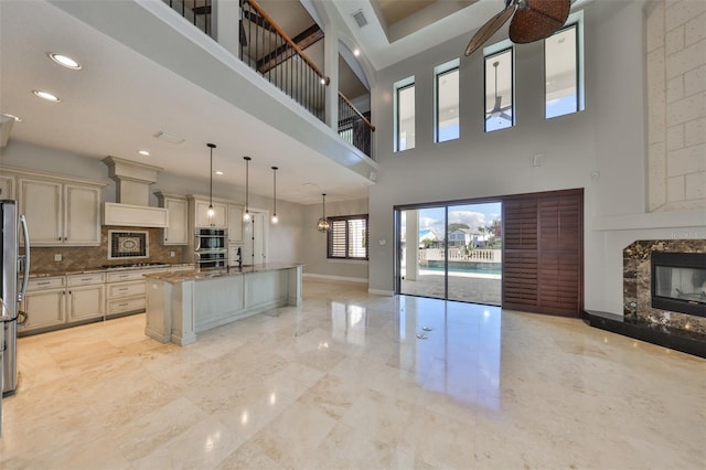 kitchen with baseboards, open floor plan, appliances with stainless steel finishes, cream cabinetry, and light stone countertops