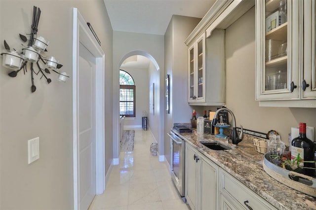 interior space with glass insert cabinets, baseboards, arched walkways, a sink, and light stone counters