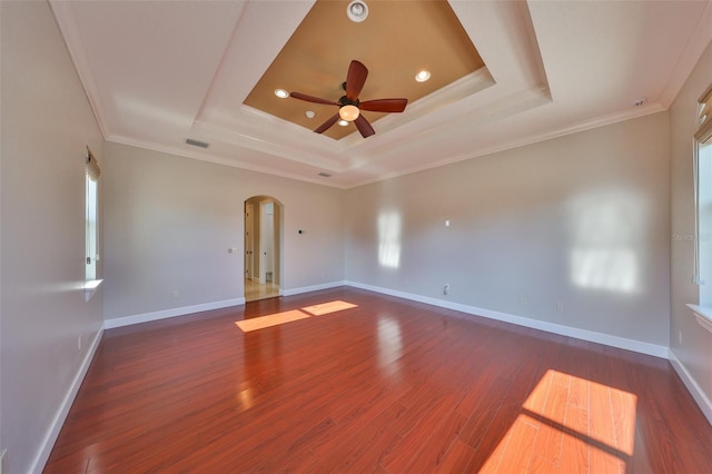 unfurnished room with visible vents, a tray ceiling, ceiling fan, arched walkways, and wood finished floors