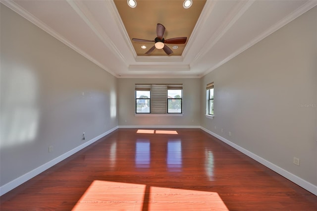 empty room with a tray ceiling, wood finished floors, ceiling fan, and baseboards