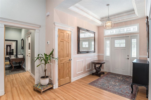 entryway with a decorative wall, crown molding, wood finished floors, a tray ceiling, and an inviting chandelier