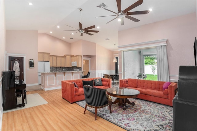 living area with visible vents, wainscoting, light wood-style flooring, ceiling fan, and high vaulted ceiling