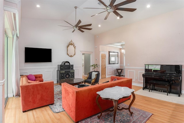 living area with wainscoting, ceiling fan, wood finished floors, vaulted ceiling, and a decorative wall