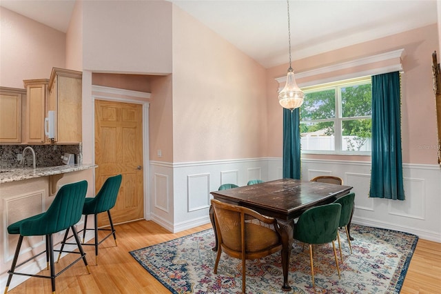 dining room featuring a wainscoted wall, light wood-style flooring, and vaulted ceiling