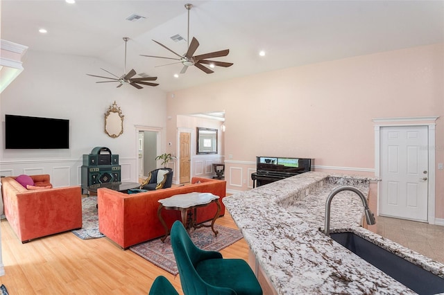 interior space with light wood finished floors, lofted ceiling, visible vents, a decorative wall, and wainscoting