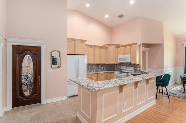 kitchen with light stone counters, a breakfast bar, a sink, white appliances, and a peninsula