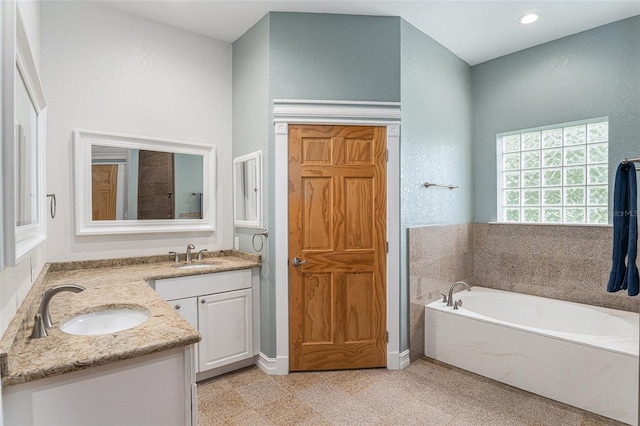 bathroom with recessed lighting, a garden tub, a sink, and double vanity