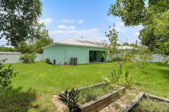 back of house with central air condition unit, a garden, a lawn, and a fenced backyard