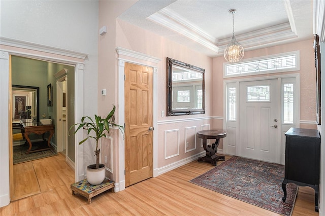 foyer entrance featuring a raised ceiling, a wainscoted wall, ornamental molding, wood finished floors, and a decorative wall