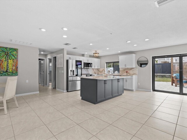 kitchen featuring light tile patterned floors, appliances with stainless steel finishes, white cabinets, a kitchen island, and decorative backsplash