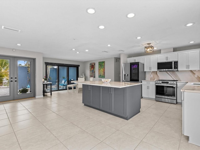 kitchen featuring appliances with stainless steel finishes, white cabinetry, backsplash, light stone countertops, and a kitchen island